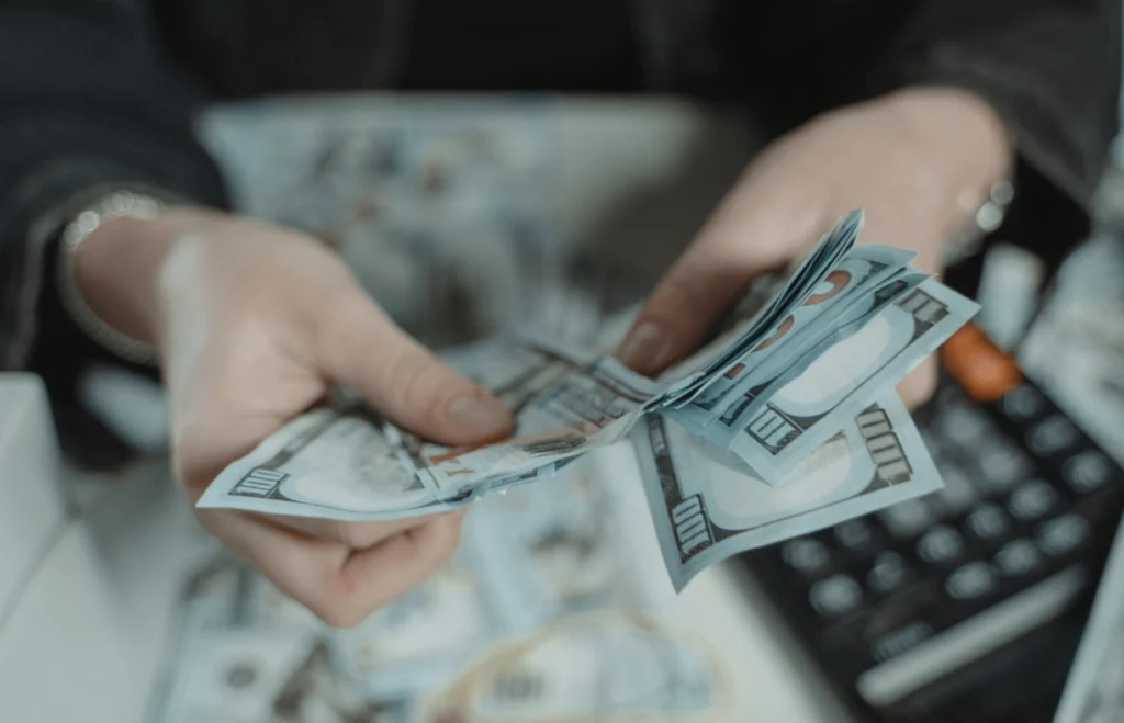 Hands counting a stack of notes with a calculator and currency in the background.