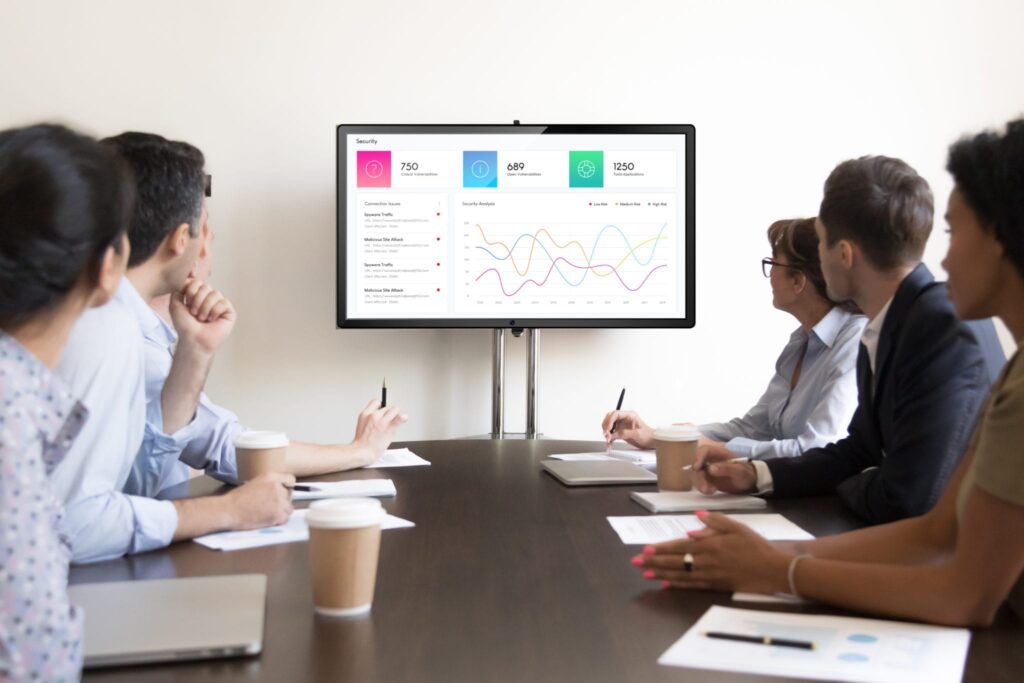 Group of professionals reviewing dashboard metrics on screen during meeting in modern conference room
