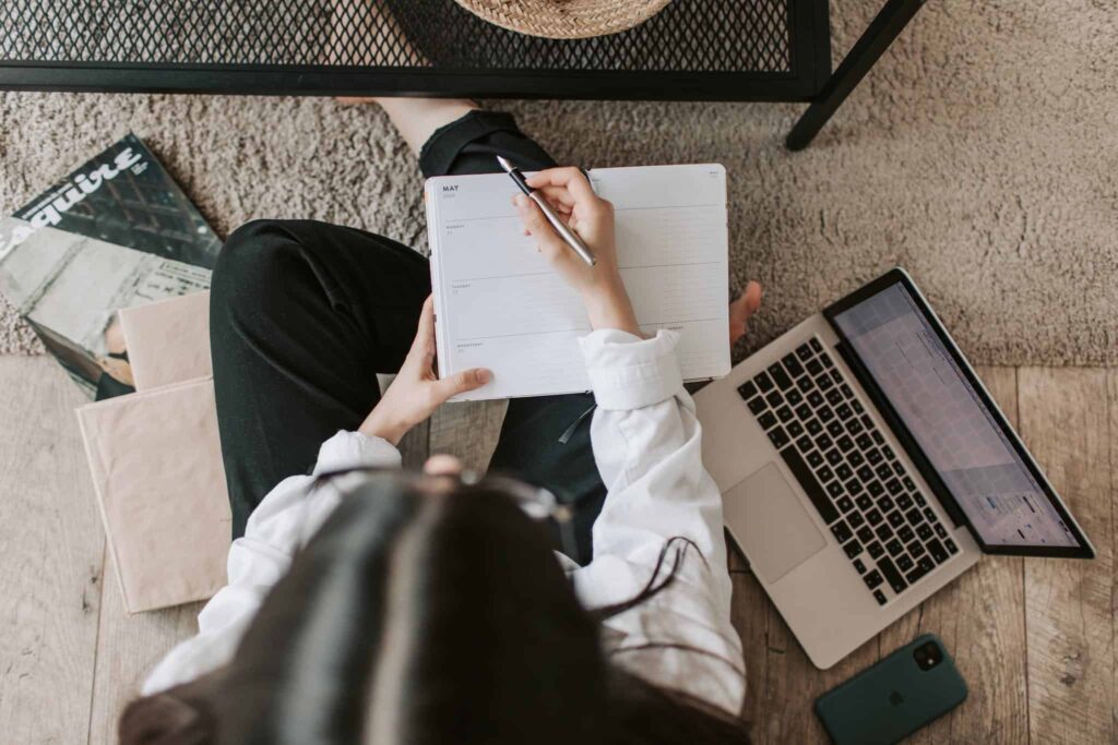 Person sitting on floor with laptop, smartphone, and weekly planner in casual workspace setting