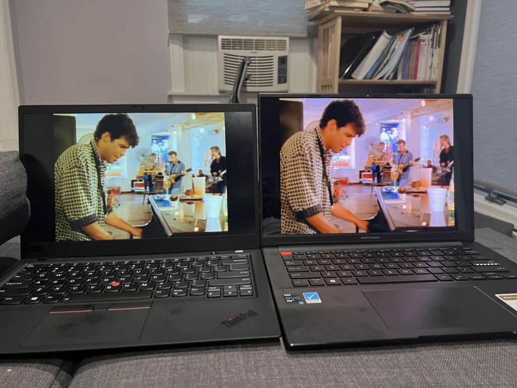 Two laptops side by side on couch displaying same video scene for screen quality comparison