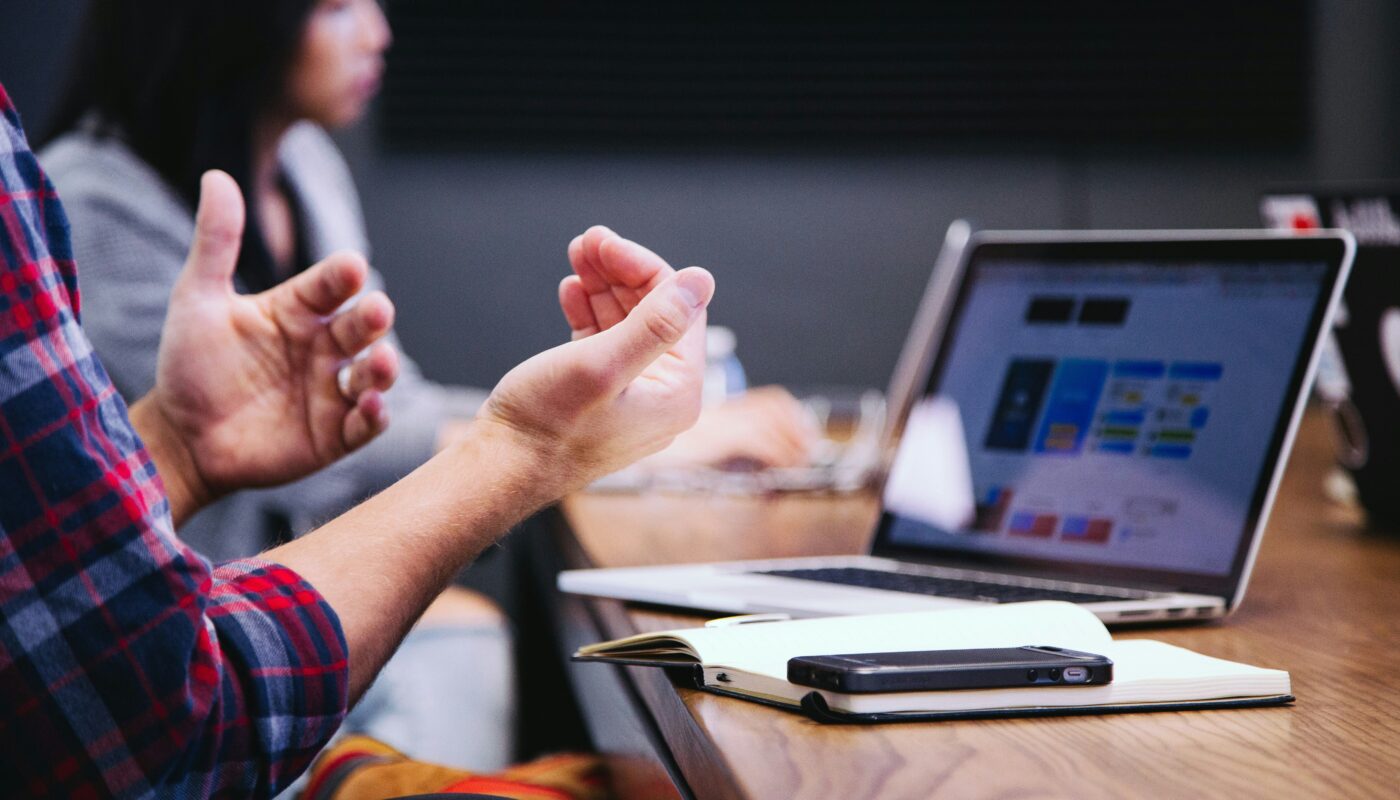 Tech blogger gesturing during collaborative session with laptop, smartphone, and notebook in modern workspace