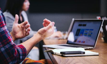 Tech blogger gesturing during collaborative session with laptop, smartphone, and notebook in modern workspace