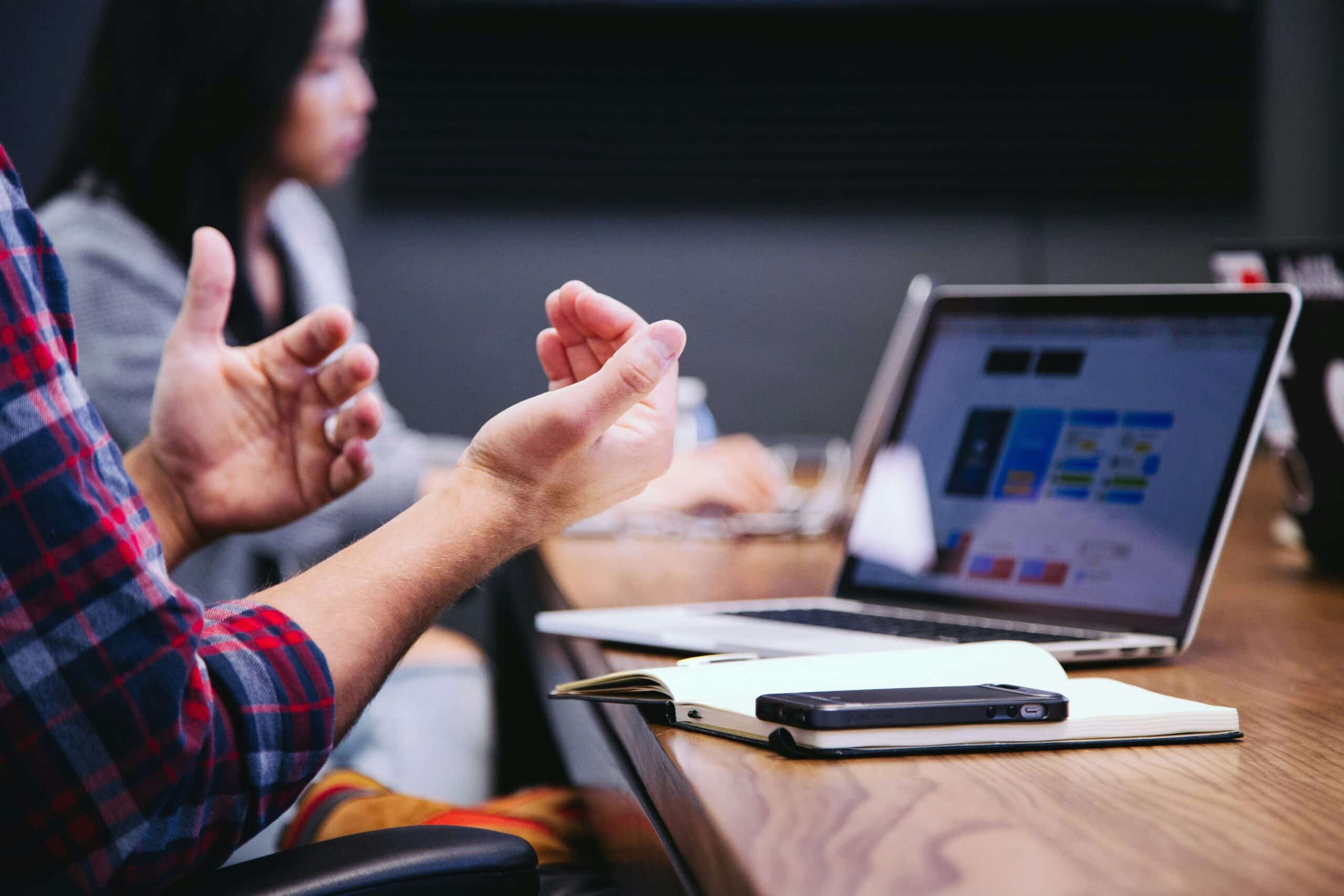 Tech blogger gesturing during collaborative session with laptop, smartphone, and notebook in modern workspace